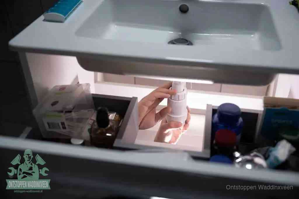 Een pompfles met zeep boven een wastafel, de heet water en afwasmiddel-methode om een vetprop in de afvoer los te maken in Waddinxveen