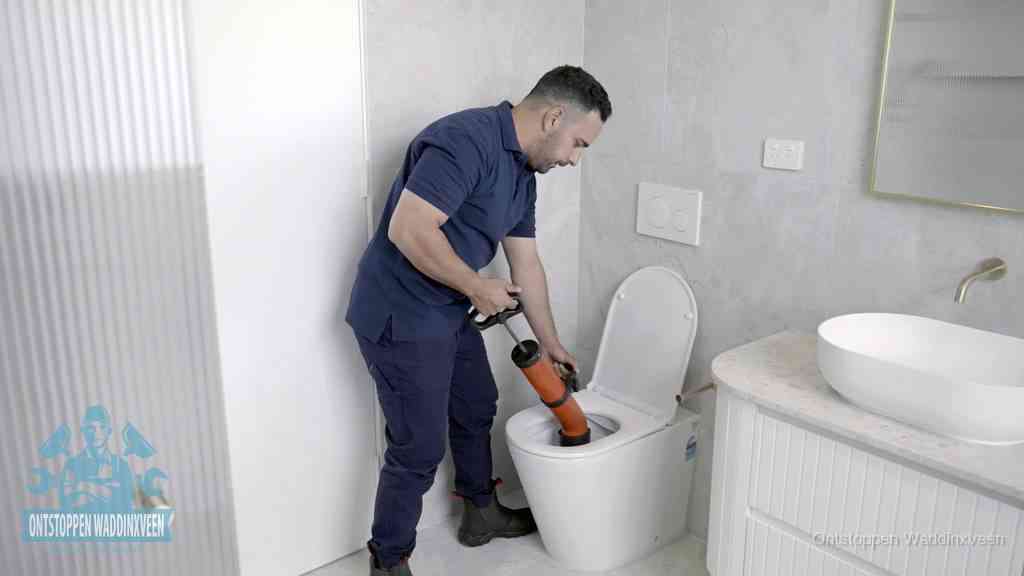 Een monteur buigt over een wandcloset en duwt met de hand een persluchtontstopper in de toiletpot om de verstopping handmatig los te maken in Waddinxveen