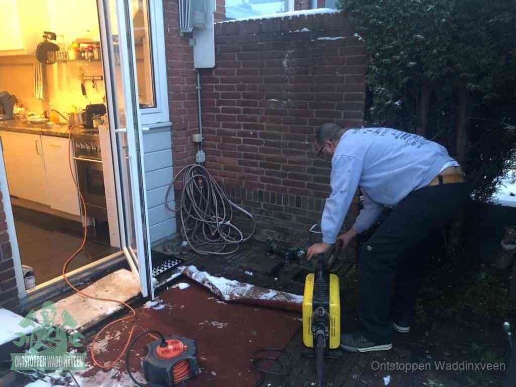 Een monteur werkt buiten bij een open riool-/grondput met een elektrische ontstoppingsmachine om een verborgen afvoerprobleem op te sporen in Waddinxveen
