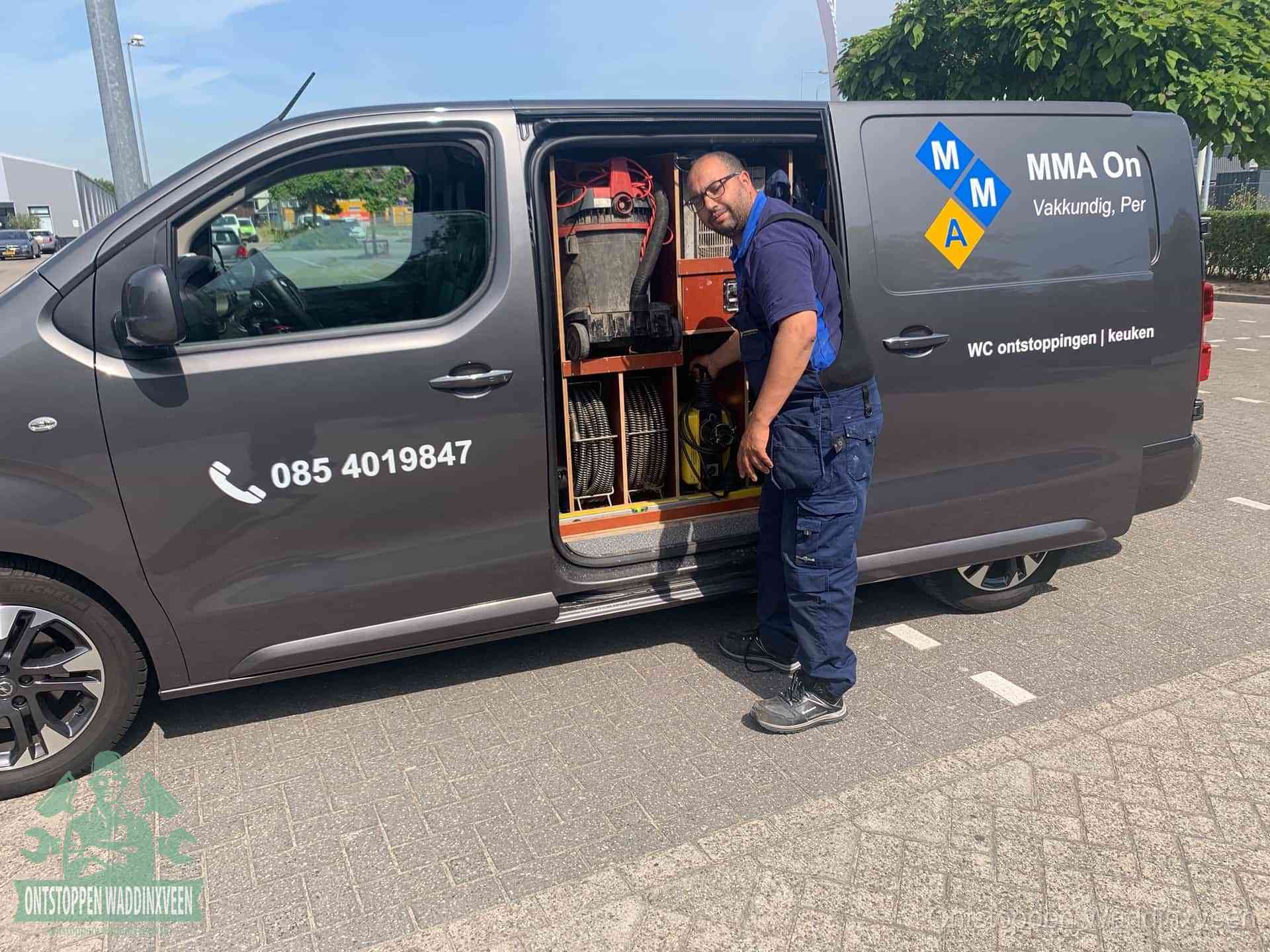 Een monteur bij de open schuifdeur van zijn bedrijfsbus op een parkeerplaats, klaar om de oorzaak van terugkerende afvoerverstoppingen aan te pakken in Waddinxveen