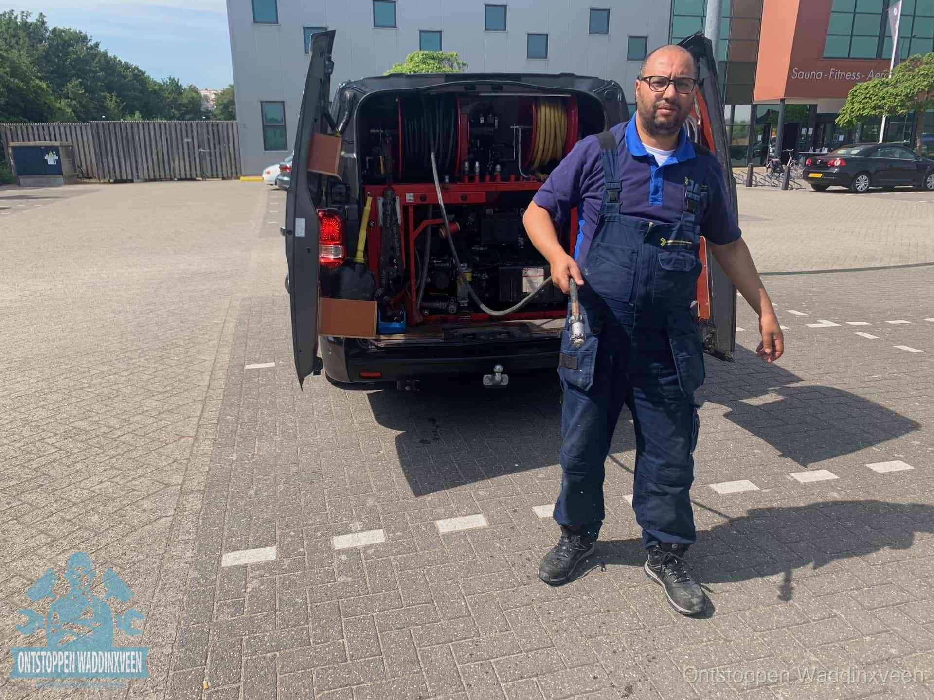 Een monteur bij zijn bestelbus met een hogedruk- en rioolreinigingsunit, klaar om de oorzaak van terugkerende wc-verstoppingen aan te pakken in Waddinxveen