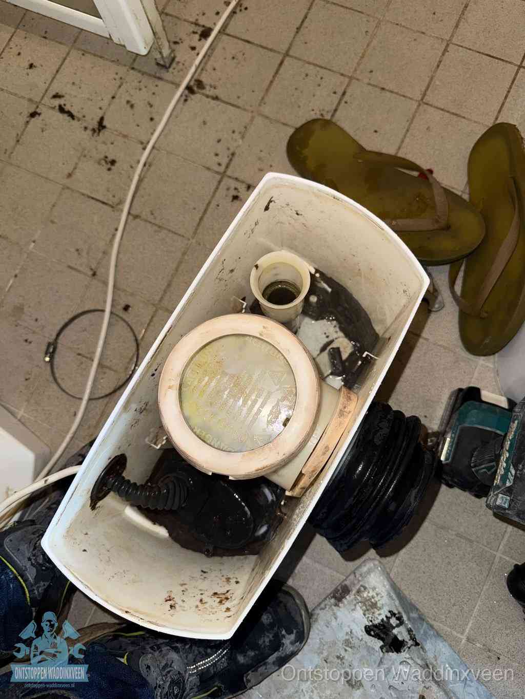 Een gedemonteerde toiletpot op de vloer met ontstoppingsveer en gereedschap ernaast, het verwijderen van een vastzittend voorwerp uit de wc in Waddinxveen