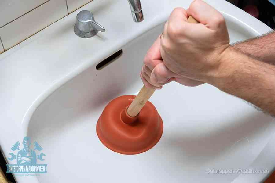 Twee handen gebruiken een rode rubberen plopper op een sanitair-afvoer om het toilet te ontstoppen in Waddinxveen