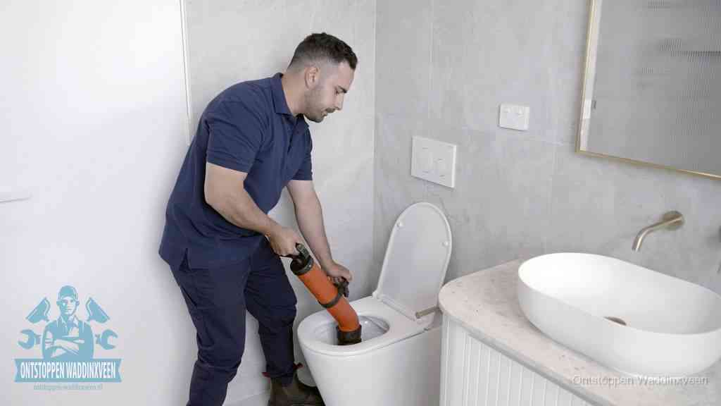 Een man gebruikt een handmatige luchtdruk-ontstopper in een modern betegeld toilet om zelf de wc te ontstoppen in Waddinxveen